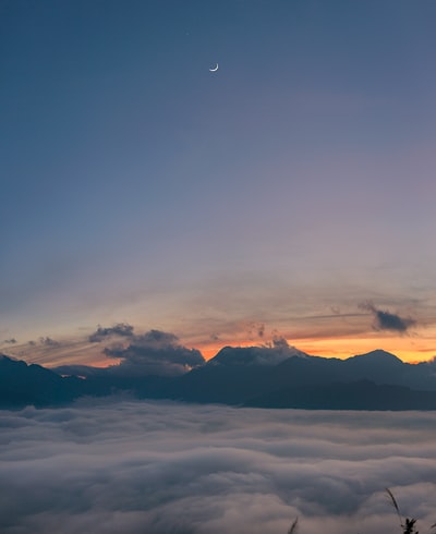 白色的新月在蓝色的夕阳天空中，云彩在下面盘旋